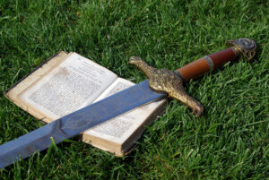 Sword laying on book, on grass.